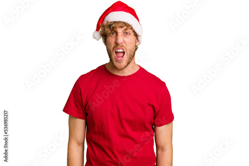 Young caucasian man wearing a Christmas Santa hat isolated on white background screaming very angry and aggressive.