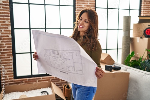 Young latin woman smiling confident holding house plan at hew home