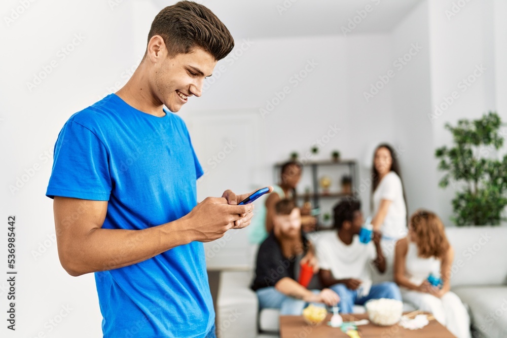 Group of young friends smiling happy sitting on the sofa. Woman using smartphone at home.