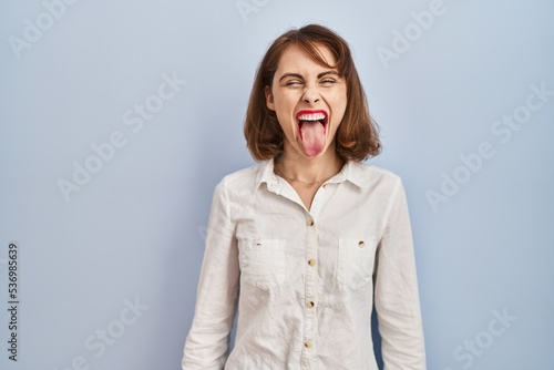 Young beautiful woman standing casual over blue background sticking tongue out happy with funny expression. emotion concept.