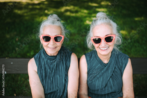 High angle view of happy senior women, twins in same clothes, smiling and posing in city park. photo