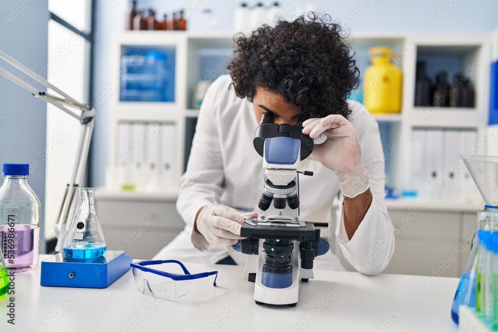 Young hispanic man wearing scientist uniform using microscope at laboratory Young hispanic man wearing scientist uniform using microscope at laboratory
