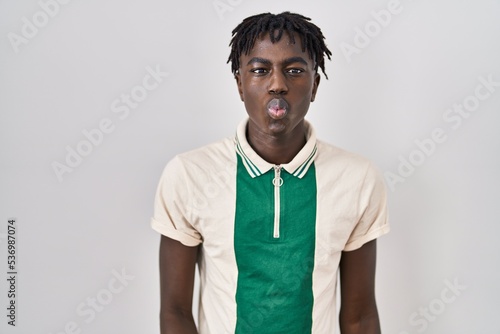 African man with dreadlocks standing over isolated background making fish face with lips, crazy and comical gesture. funny expression.