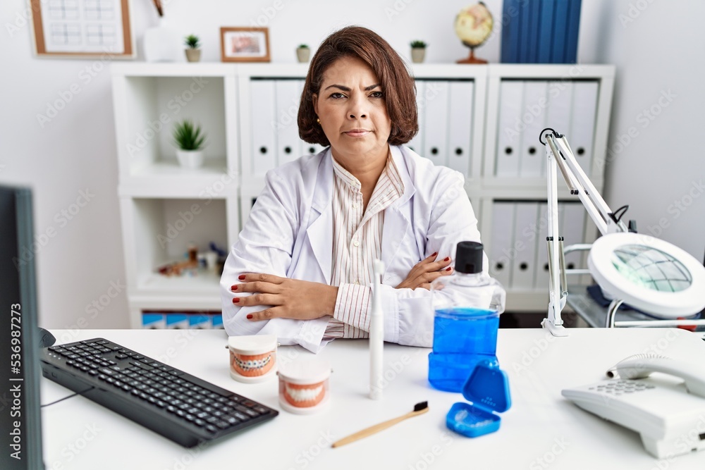 Middle age hispanic dentist woman working at medical clinic skeptic and nervous, disapproving expression on face with crossed arms. negative person. Middle age hispanic dentist woman working at medical clinic skeptic and nervous, disapproving expression on face with crossed arms. negative person.
