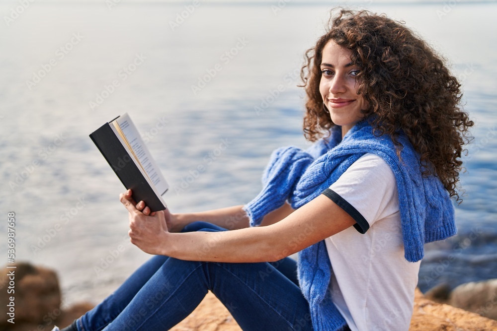Young hispanic woman smiling confident reading book at seaside