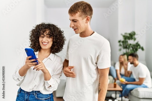 Two young friends standing and using smartphone at home.