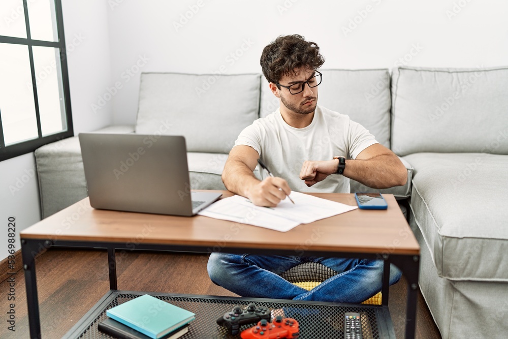 Hispanic man doing papers at home checking the time on wrist watch, relaxed and confident Hispanic man doing papers at home checking the time on wrist watch, relaxed and confident