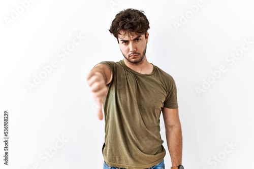 Hispanic man standing over isolated white background looking unhappy and angry showing rejection and negative with thumbs down gesture. bad expression.