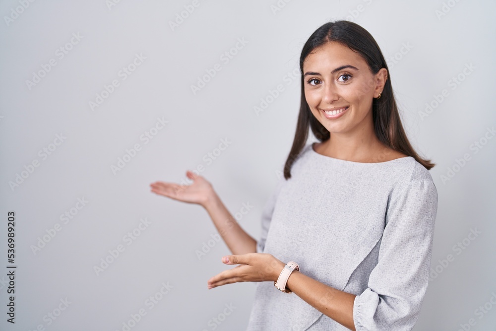 Young hispanic woman standing over white background inviting to enter smiling natural with open hand Young hispanic woman standing over white background inviting to enter smiling natural with open hand