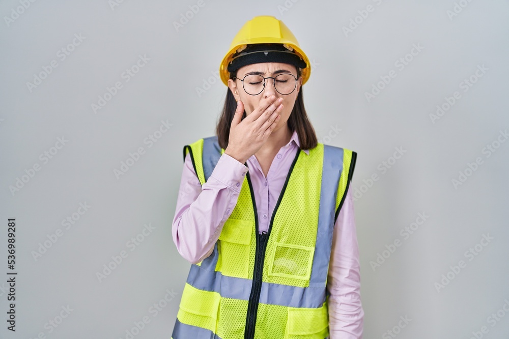 Hispanic girl wearing builder uniform and hardhat bored yawning tired covering mouth with hand. restless and sleepiness. Hispanic girl wearing builder uniform and hardhat bored yawning tired covering mouth with hand. restless and sleepiness.