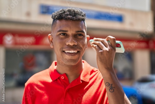 Young latin man smiling confident listening audio message by the smartphone at street