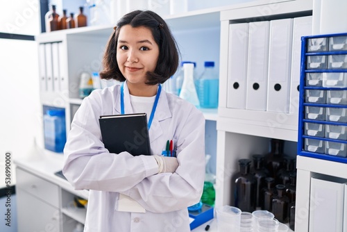 Young hispanic woman working at scientist laboratory smiling looking to the side and staring away thinking.