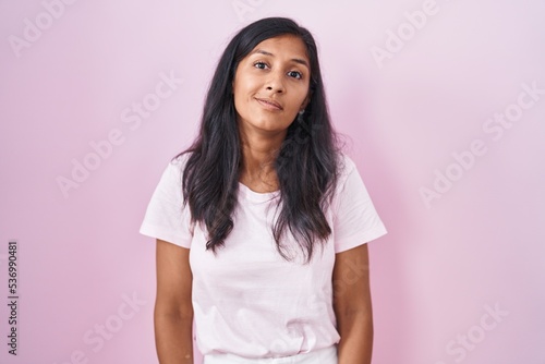 Young hispanic woman standing over pink background relaxed with serious expression on face. simple and natural looking at the camera.