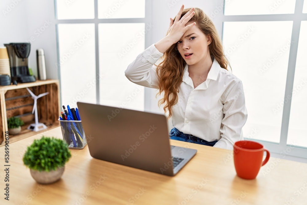 Young caucasian woman working at the office using computer laptop surprised with hand on head for mistake, remember error. forgot, bad memory concept. Young caucasian woman working at the office using computer laptop surprised with hand on head for mistake, remember error. forgot, bad memory concept.