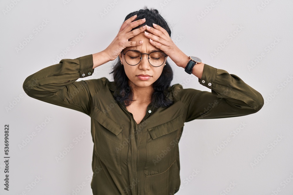 Hispanic woman with dark hair standing over isolated background suffering from headache desperate and stressed because pain and migraine. hands on head. Hispanic woman with dark hair standing over isolated background suffering from headache desperate and stressed because pain and migraine. hands on head.