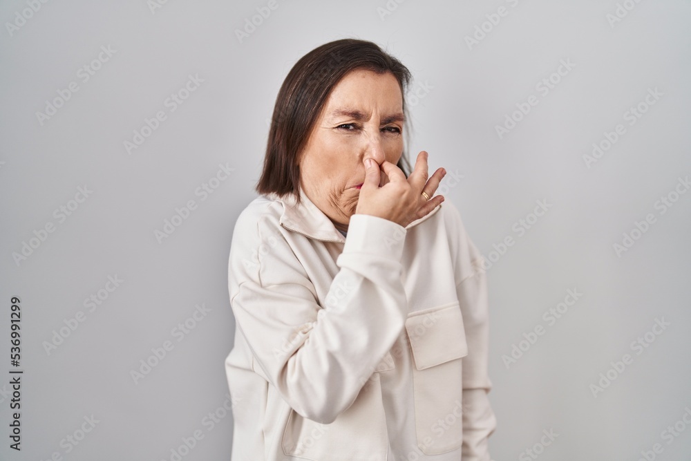 Middle age hispanic woman standing over isolated background smelling something stinky and disgusting, intolerable smell, holding breath with fingers on nose. bad smell Middle age hispanic woman standing over isolated background smelling something stinky and disgusting, intolerable smell, holding breath with fingers on nose. bad smell