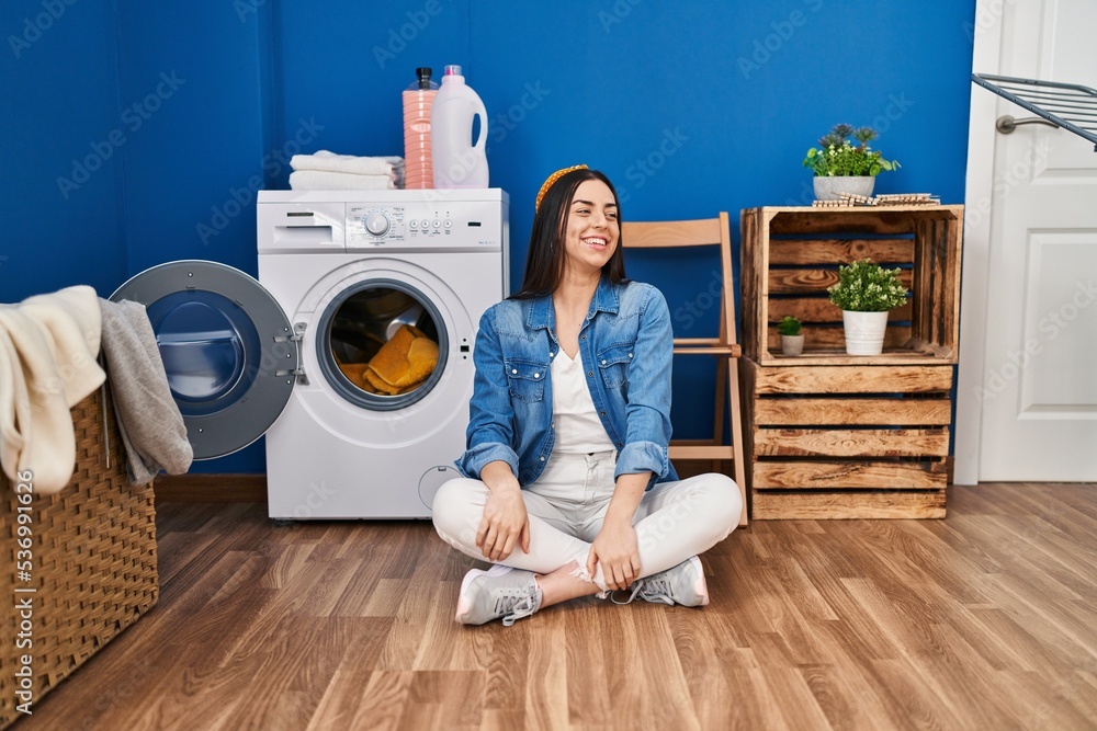 Hispanic woman doing laundry sitting on the floor looking away to side with smile on face, natural expression. laughing confident. Hispanic woman doing laundry sitting on the floor looking away to side with smile on face, natural expression. laughing confident.