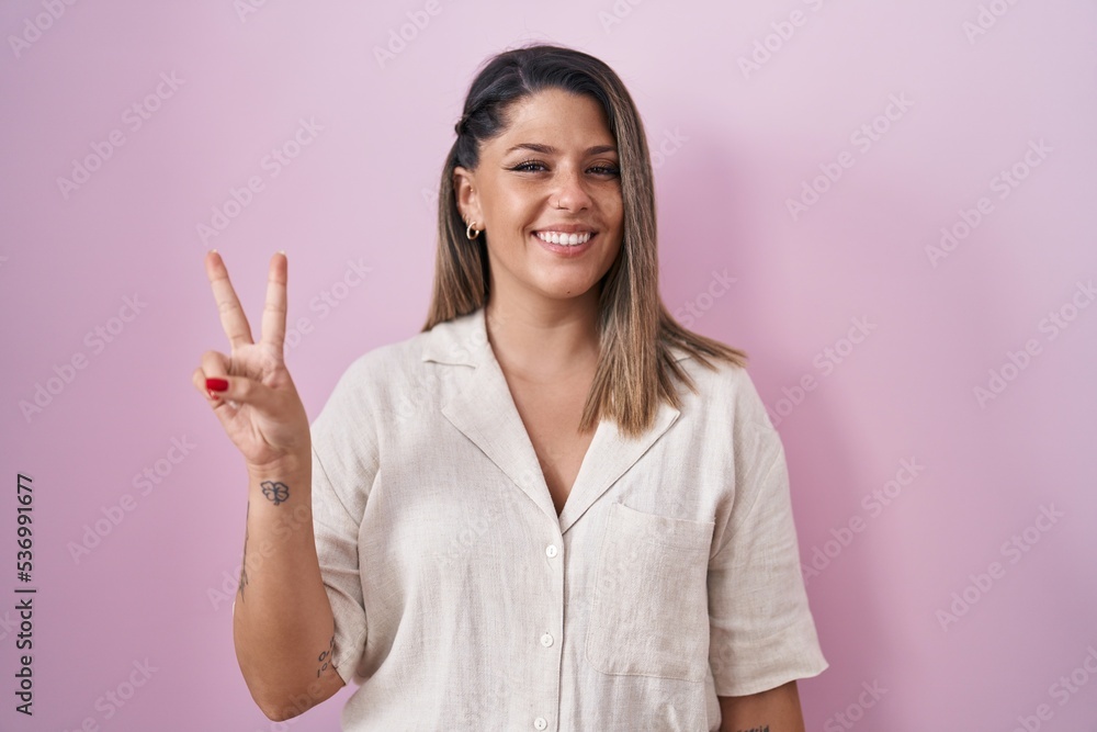 Blonde woman standing over pink background showing and pointing up with fingers number two while smiling confident and happy. Blonde woman standing over pink background showing and pointing up with fingers number two while smiling confident and happy.