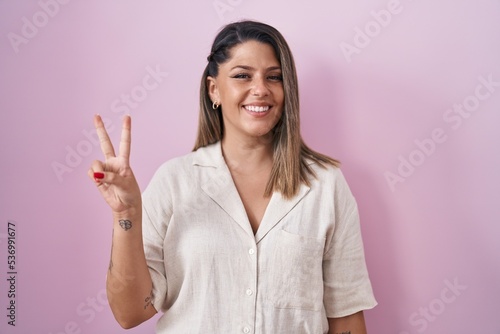 Blonde woman standing over pink background showing and pointing up with fingers number two while smiling confident and happy.