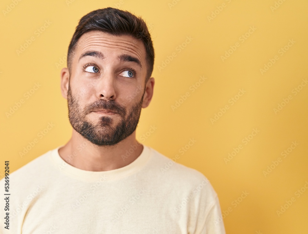 Handsome hispanic man standing over yellow background smiling looking to the side and staring away thinking. Handsome hispanic man standing over yellow background smiling looking to the side and staring away thinking.