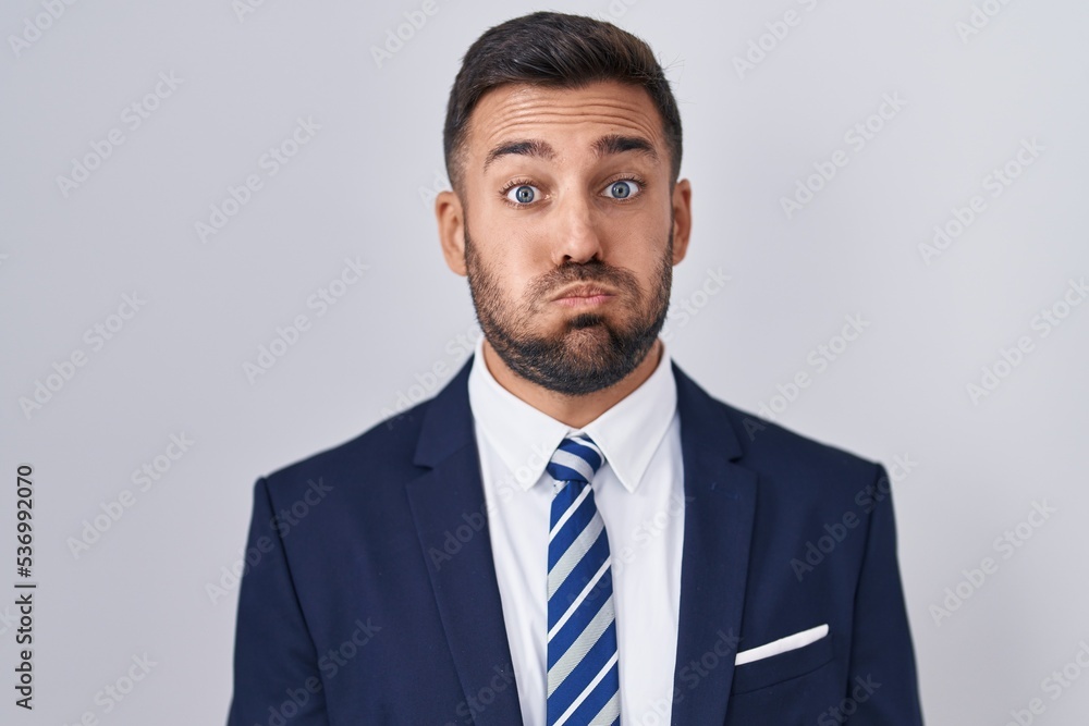 Handsome hispanic man wearing suit and tie puffing cheeks with funny face. mouth inflated with air, crazy expression. Handsome hispanic man wearing suit and tie puffing cheeks with funny face. mouth inflated with air, crazy expression.