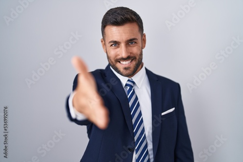 Handsome hispanic man wearing suit and tie smiling friendly offering handshake as greeting and welcoming. successful business.