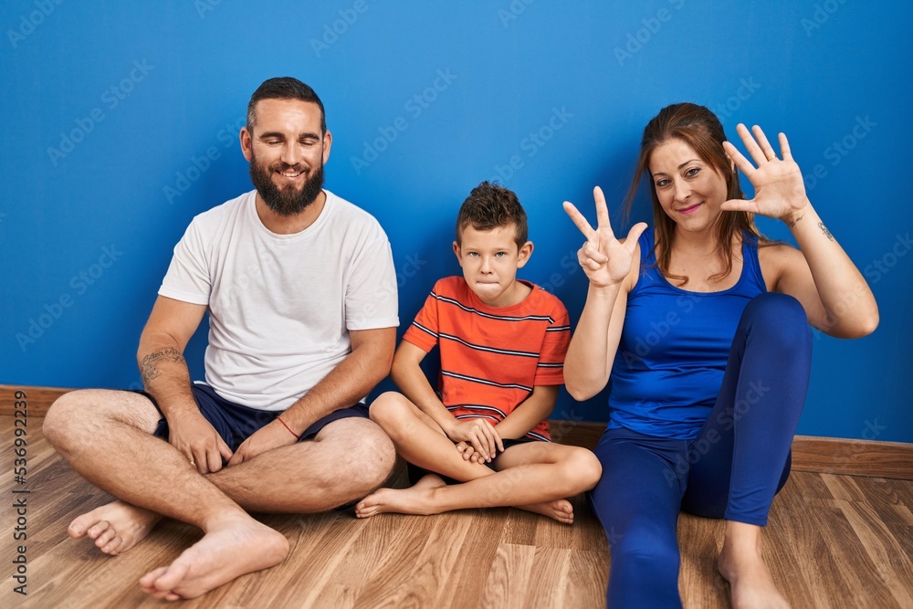 Family of three sitting on the floor at home showing and pointing up with fingers number eight while smiling confident and happy. Family of three sitting on the floor at home showing and pointing up with fingers number eight while smiling confident and happy.