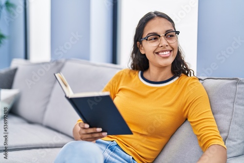 Young african american woman reading book sitting on sofa at home
