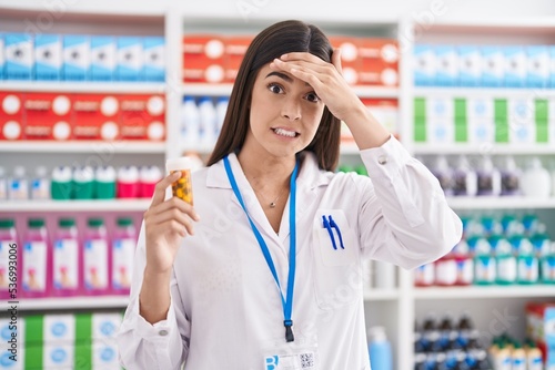 Hispanic woman working at pharmacy drugstore holding pills stressed and frustrated with hand on head, surprised and angry face