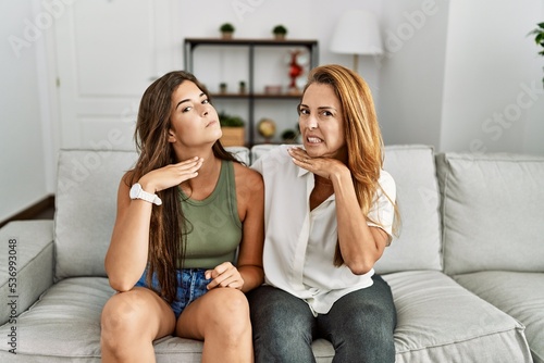 Mother and daughter together sitting on the sofa at home cutting throat with hand as knife, threaten aggression with furious violence