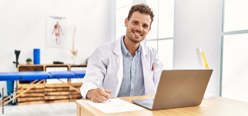 Young hispanic man wearing physiotherapist uniform writing on document at clinic Young hispanic man wearing physiotherapist uniform writing on document at clinic