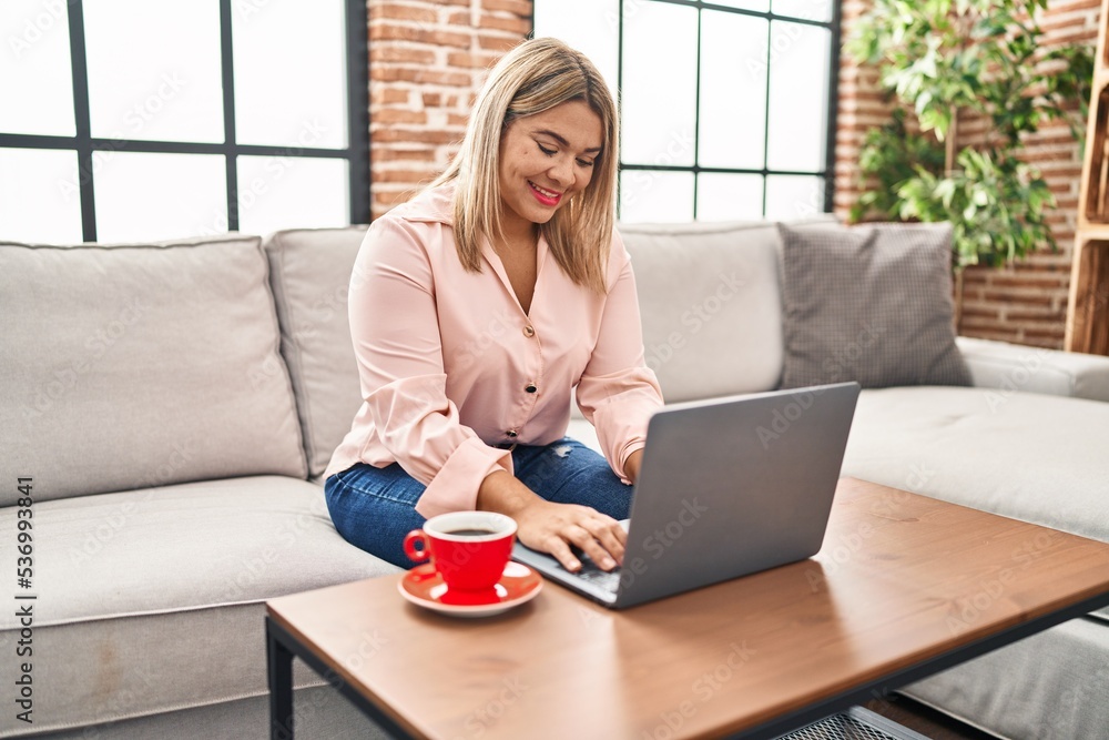 Young hispanic woman using laptop and drinking coffee sitting on sofa at home Young hispanic woman using laptop and drinking coffee sitting on sofa at home