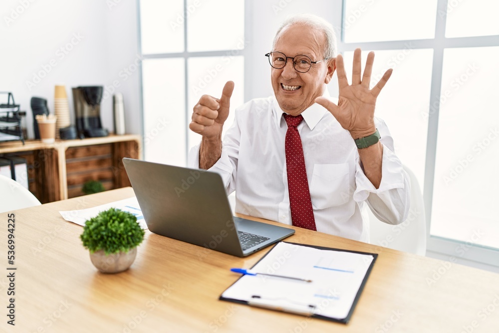 Senior man working at the office using computer laptop showing and pointing up with fingers number six while smiling confident and happy. Senior man working at the office using computer laptop showing and pointing up with fingers number six while smiling confident and happy.