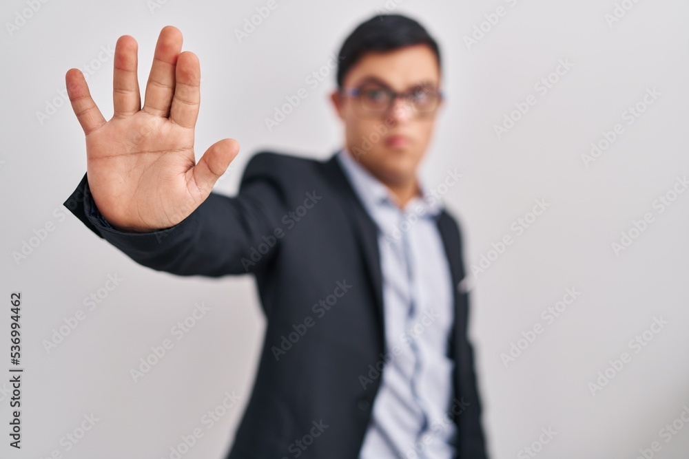Young hispanic man with down syndrome wearing business style doing stop sing with palm of the hand. warning expression with negative and serious gesture on the face. Young hispanic man with down syndrome wearing business style doing stop sing with palm of the hand. warning expression with negative and serious gesture on the face.