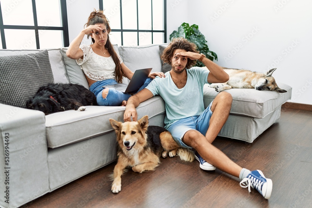 Young hispanic couple with dogs relaxing at home worried and stressed about a problem with hand on forehead, nervous and anxious for crisis