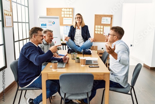 Businesswoman enjoys meditating during meeting. Sitting on desk near arguing partners at the office.