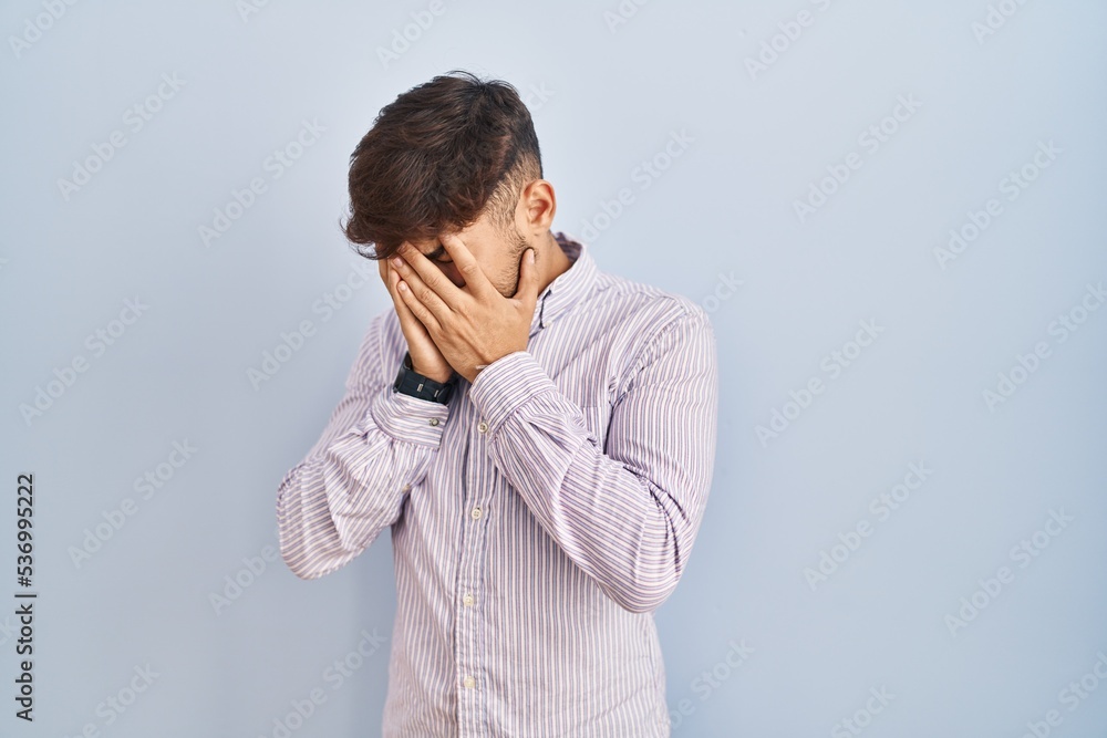 Arab man with beard standing over blue background with sad expression covering face with hands while crying. depression concept. Arab man with beard standing over blue background with sad expression covering face with hands while crying. depression concept.