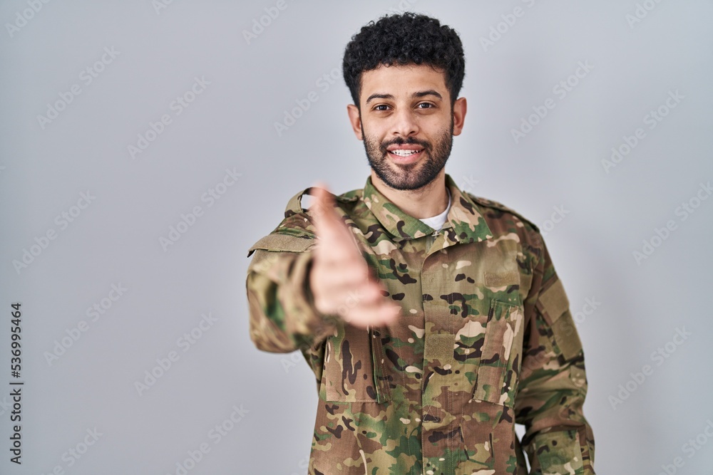 Arab man wearing camouflage army uniform smiling cheerful offering palm hand giving assistance and acceptance.