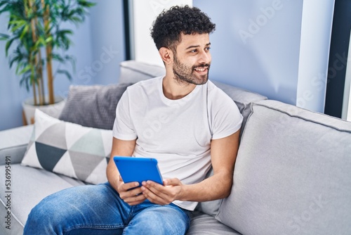 Young arab man using touchpad sitting on sofa at home