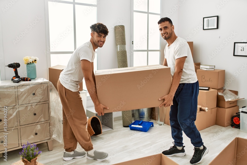Two hispanic men couple smiling confident holding cardboard box at new home Two hispanic men couple smiling confident holding cardboard box at new home
