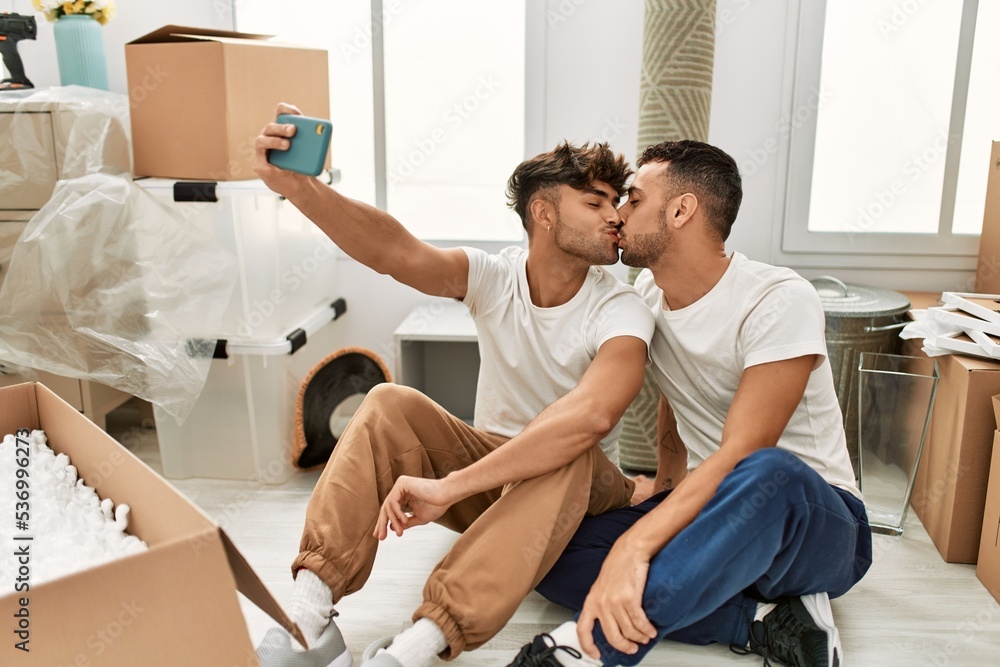 Obraz premium Two hispanic men couple kissing and make selfie by the smartphone at new home