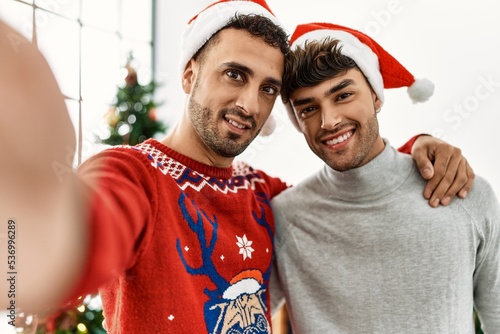 Two hispanic men couple make selfie by the camera standing by christmas tree at home