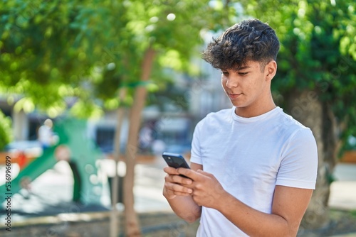 Young hispanic teenager smiling confident using smartphone at park