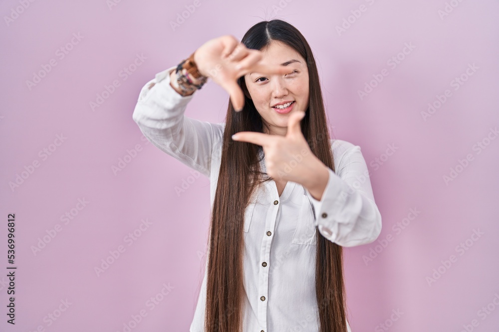 Chinese young woman standing over pink background smiling making frame with hands and fingers with happy face. creativity and photography concept. Chinese young woman standing over pink background smiling making frame with hands and fingers with happy face. creativity and photography concept.