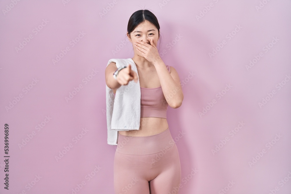 Chinese young woman wearing sportswear and towel laughing at you, pointing finger to the camera with hand over mouth, shame expression Chinese young woman wearing sportswear and towel laughing at you, pointing finger to the camera with hand over mouth, shame expression