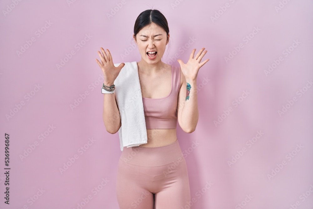 Chinese young woman wearing sportswear and towel celebrating mad and crazy for success with arms raised and closed eyes screaming excited. winner concept Chinese young woman wearing sportswear and towel celebrating mad and crazy for success with arms raised and closed eyes screaming excited. winner concept