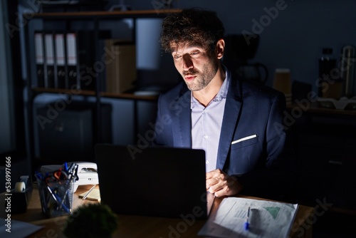 Hispanic young man working at the office at night making fish face with lips, crazy and comical gesture. funny expression.