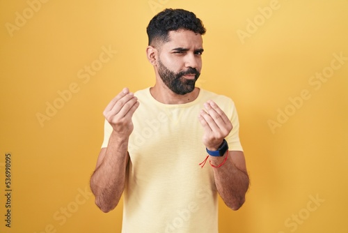 Hispanic man with beard standing over yellow background doing money gesture with hands, asking for salary payment, millionaire business © Krakenimages.com