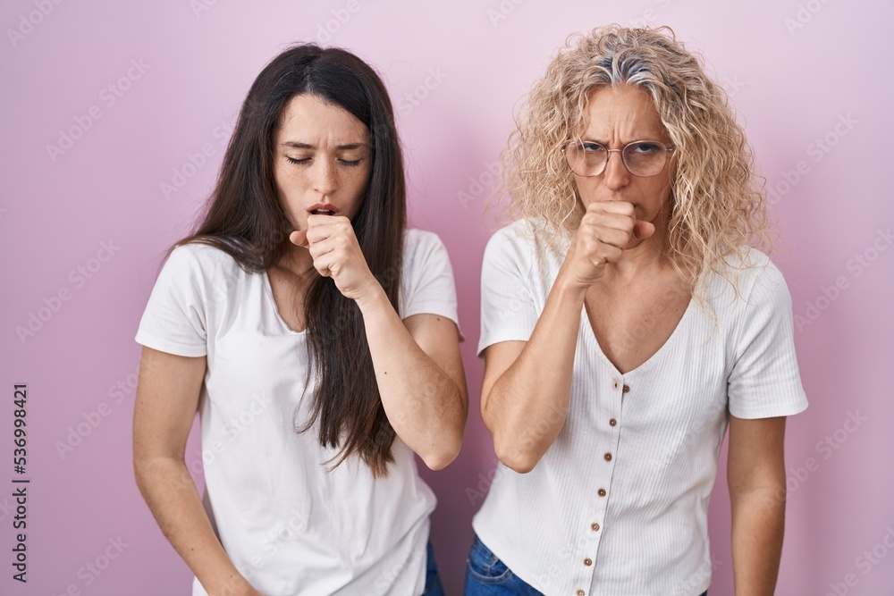Mother and daughter standing together over pink background feeling unwell and coughing as symptom for cold or bronchitis. health care concept. Mother and daughter standing together over pink background feeling unwell and coughing as symptom for cold or bronchitis. health care concept.