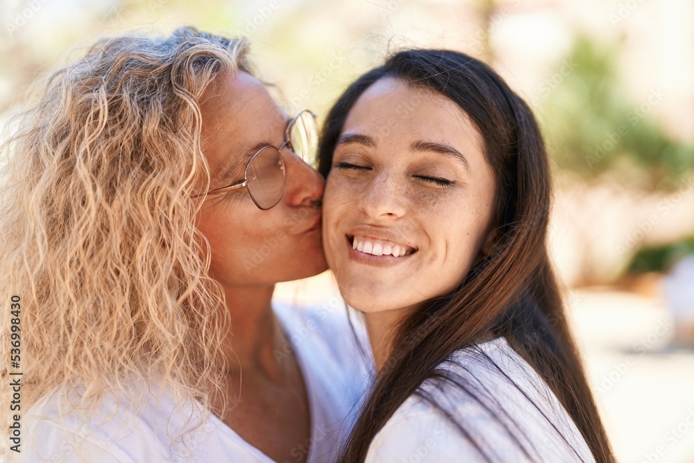 Two women mother and daughter standing together kissing at park Two women mother and daughter standing together kissing at park